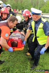 Na zdjęciu ratownik medyczny, dwóch strażaków i policjant niosą na noszach ranną osobę.